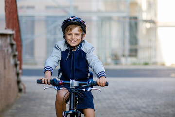 Schoolkid boy in safety helmet riding with bike in the city with backpack. Happy child in colorful...