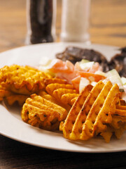 Dinner with well cooked lamb chops on the bone, potato lattice shape chips and fresh salad with cream. High quality products. Tasty properly meal. Fine simple food.