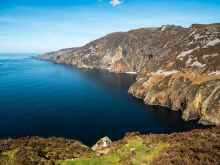 Stunning picturesque view on Slieve league cliffs, county Donegal, Ireland. Warm sunny day. Irish landscape scene. Blue cloudy sky and ocean surface, rough and tall cliffs.