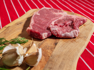 Fresh uncooked T bone steak with fresh dill and garlic cloves on wooden cutting board and on classic red and white stripe table cloth. High quality beef meat product. Butcher craft.