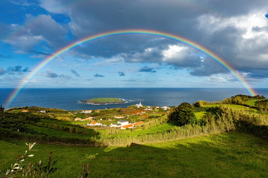 Breathtaking view of the amall village and lighthouse at S&atilde;o Jorge island in Azores with huge rainbow in the sky Portugal