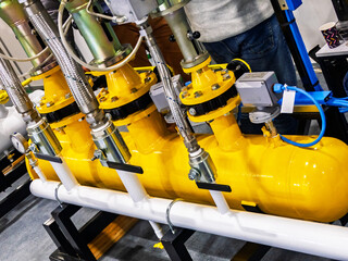 A close-up of an industrial gas or fluid control system. Yellow cylindrical tank is the...
