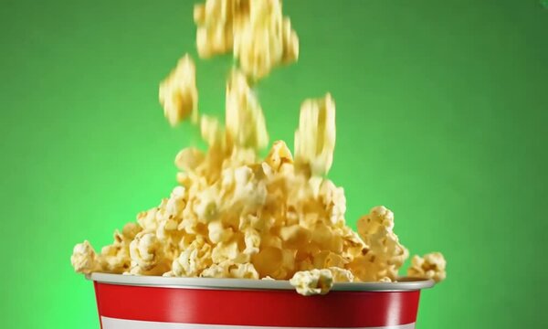 Popcorn falling out of a red-white striped bucket on a green background, nice background
