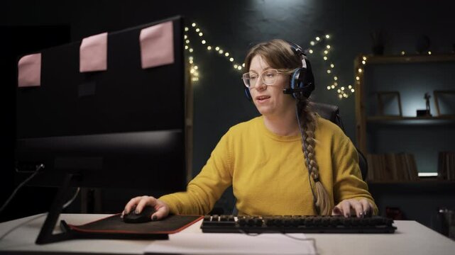 adult female gamer in glasses playing a round in online video game on personal computer. Professional player enjoying championship scratching head and spreading arms gesture of justification