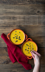 Two bowls of soup with seeds on top, one is orange and the other is yellow. A hand is reaching for the yellow bowl