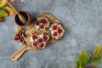 A plate of fruit with a wooden board underneath it. The plate has three slices of fruit, including two slices of figs and one slice of apple. There is also a jar of honey on the table