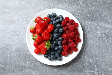 Different fresh ripe berries in bowl on gray table, top view