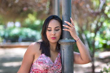 brunette, young and beautiful woman holds an iron lamppost with one hand and puts her face next to...