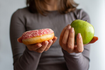 A girl holding an apple and a donut. The choice between healthy eating and junk food