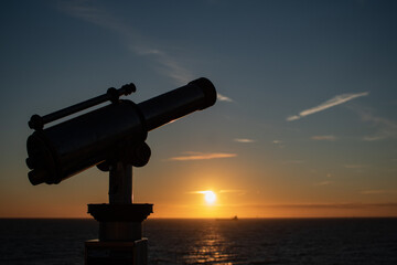 Side view of telescope at the pier in Scheveningen, focus on the foreground, blurred background. Sunset, warm light, tranquil scene. The Hague, Netherlands.