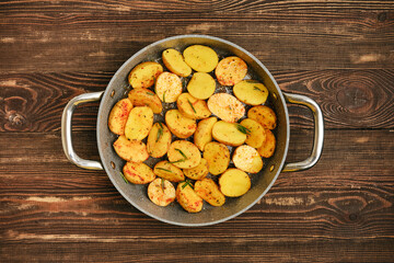 Crispy roasted potatoes with herbs prepared in a pan on a rustic wooden table