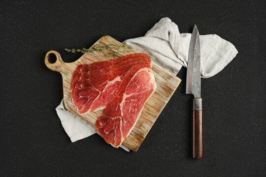 Overhead view of jamon iberico cured pork meat on a wooden cutting board, accompanied by a sharp knife