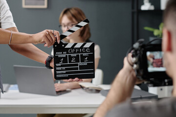 Medium clos up of unrecognizable cameraman shooting scene with woman, focus on black clapperboard in unrecognizable female hands