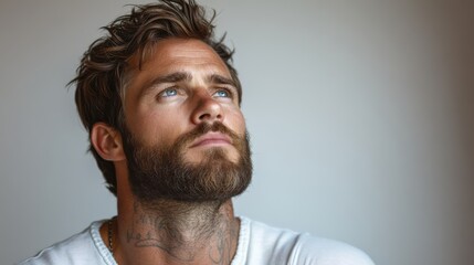 Obraz premium A contemplative man with a beard and tattoos gazes thoughtfully into the distance.