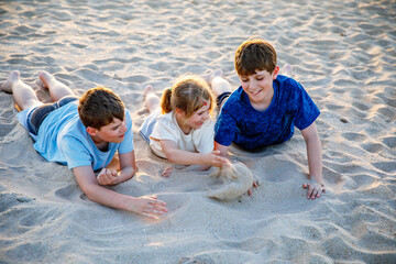 Three children playing with sand on sunset ocean beach. happy family, two school boys and one little preschool girl. Siblings having fun together. Bonding and family vacation in Andalucia, Spain