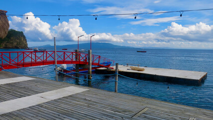 Obraz premium View of a pier on the shore of a tropical island. A boat dock with a wooden deck and a small bridge connecting the pier and a floating platform.