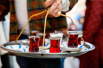 Turkish tea in traditional glass mugs on a metal tray. Street vendor selling hot tea in Istanbul, Turkey, Grand Bazaar.