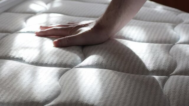 a man pushes through a new orthopedic mattress with his hand, checking its rigidity, 4k video
