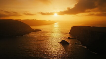 Golden sunset over a dramatic coastline with a calm ocean. Silhouetted cliffs meet the horizon.