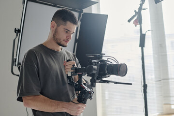 Medium close up of talented operator with massive camera enjoying shooting scene at studio