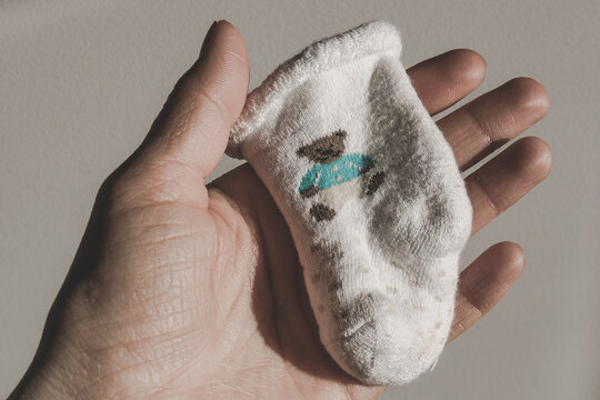 A baby sock in a woman's hand. Postnatal depression. Death of a child. Surviving loss. Childless family. Infertile woman. Infertility as a cause of divorce. Reproductive Health. Causes of Miscarriage.