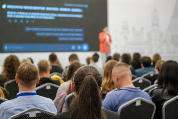 People gathered in a conference hall attending a business seminar with a speaker on stage.