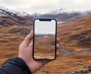 Hand holding a smartphone with a blank screen, set against the backdrop of nature and mountains