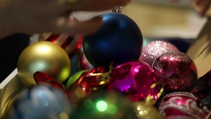 Close-up of a hand picking up shiny Christmas decorations from a festive table. Captures the tactile joy and careful selection of holiday trimming.