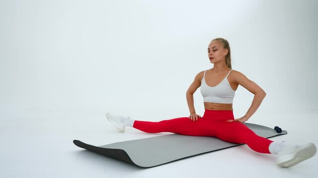 Caucasian woman doing stretching and doing side splits on white background. 