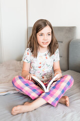 Naklejka premium Child reads a book in a bedroom. Little girl reads a bedtime story in her room. Education concept.