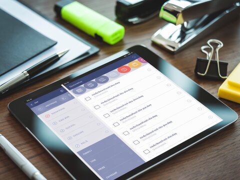 A digital tablet displaying a to-do list on a workspace with office supplies.