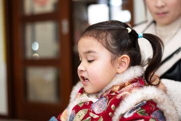 The young Chinese  mother is combing and binding her daughter's hair. Her daughter is wearing...