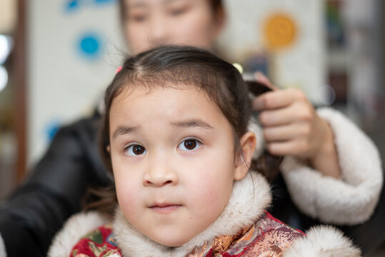 The young Chinese  mother is combing and binding her daughter's hair. Her daughter is wearing traditional Chinese clothes. They're getting ready for celebrating  Chinese New Year.