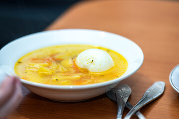 comforting bowl of noodle soup featuring tender potatoes and a perfectly cooked egg. The vibrant broth, inviting texture, and rich flavors create a warm culinary experience