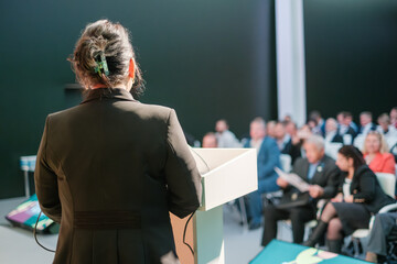 Rear view of speaker presenting to a focused audience during corporate event in modern venue. Conveying professionalism.