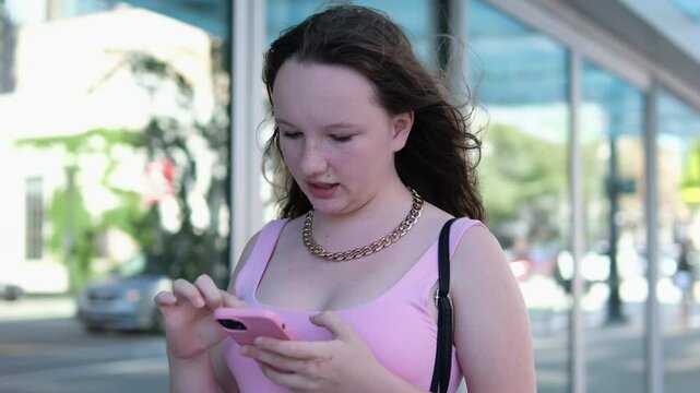 Young Hispanic Woman walking while using cell phone. Happy university student girl smiling in the city