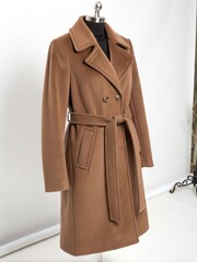Naklejka premium Stylish mocha mousse overcoat displayed on mannequin in a modern studio setting emphasizing fashion and design details