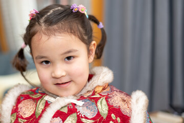 Close up portrait of cute small Chinese multiracial girl who is  ready for the celebration of Chinese New Year. She is posing for a photo in her traditional Chinese dress.