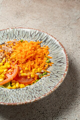 Close-up of a colorful fresh salad with grated carrot, sweet corn, tomato slices, and tuna, served on a decorative ceramic plate