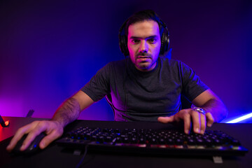 Smart gaming streamer concentrating gaming players trying to pass the level at mission completed, using headset and mic for communicate others on streaming live at neon lighting studio room. Surmise.