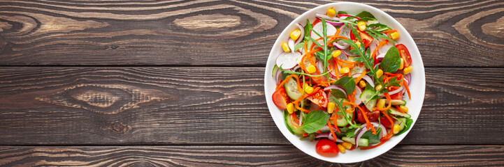 Fresh salad with vegetables. Arugula, spinach, cucumbers, tomato, onions carrots, corn andradishes in a plate on the table. Diet nutrition. Top view. Copy space