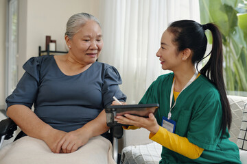 Nurse making appointment online on her touchpad and showing it to her senior patient