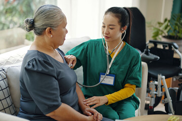 Young nurse in uniform examining heartbeat of senior patient with stethoscope