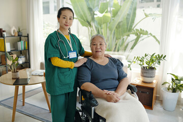 Obraz premium Portrait of caregiver standing together with senior patient in wheelchair