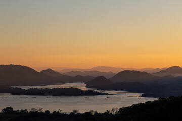 Sunrise over Lake Suchitlán in Suchitoto, El Salvador, with misty hills, calm water, and golden hues painting the horizon. Serene natural beauty ideal for travel and landscape themes.