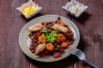 beans stewed with meat and dried fruits, spices and sauce and hummus on a wooden table