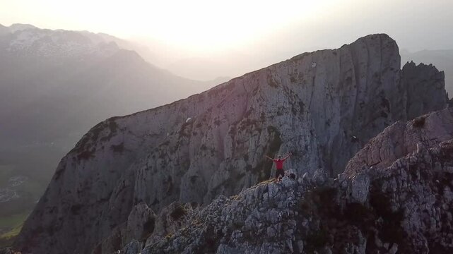 Drone clip pivoting around a man in victory pose on rugged mountain cliffs, Austria