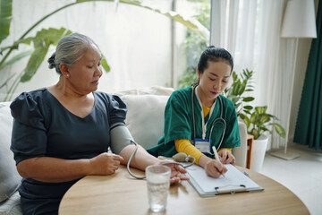 Obraz premium Nurse doing medical exam at home while visiting to senior woman