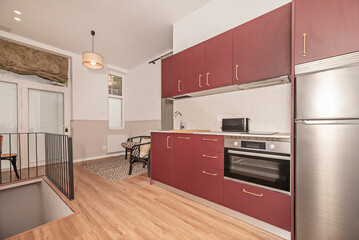 Kitchen equipped with cream stone effect countertop, stainless steel appliances and red wood cabinets