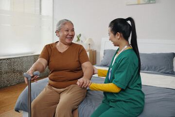 Social worker sitting on bed in the room and talking to senior woman at home